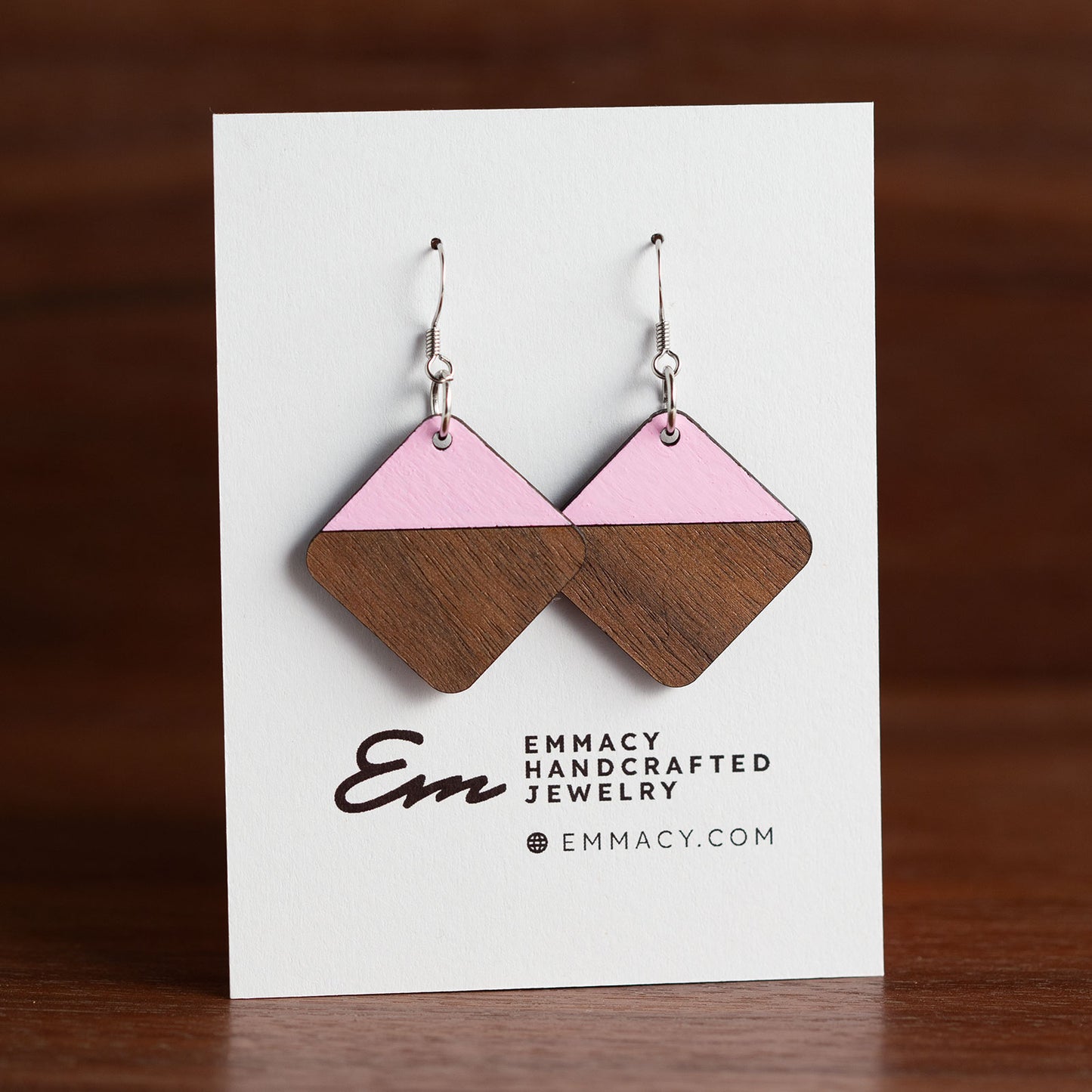 Laser cut wooden dangle earrings in the shaper of rounded diamonds with the top half painted pink.