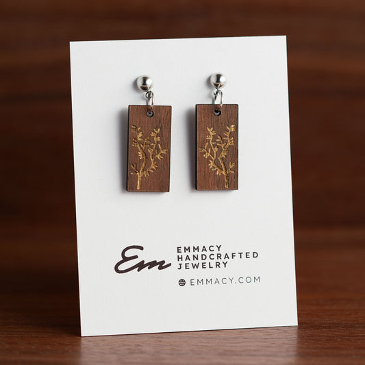 Laser cut wooden dangle earrings in the shape of a rounded rectangle with engraved branches.