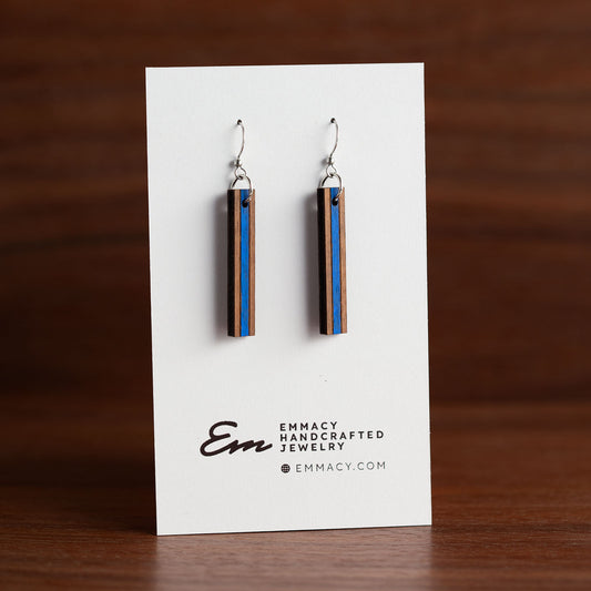 Laser cut wooden dangle earrings in the shape of a thin rectangle with a blue painted stripe in the middle third.