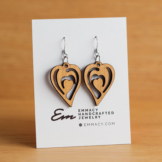 Laser cut wooden dangle earrings in the shape of a curvy heart with curved cutouts.