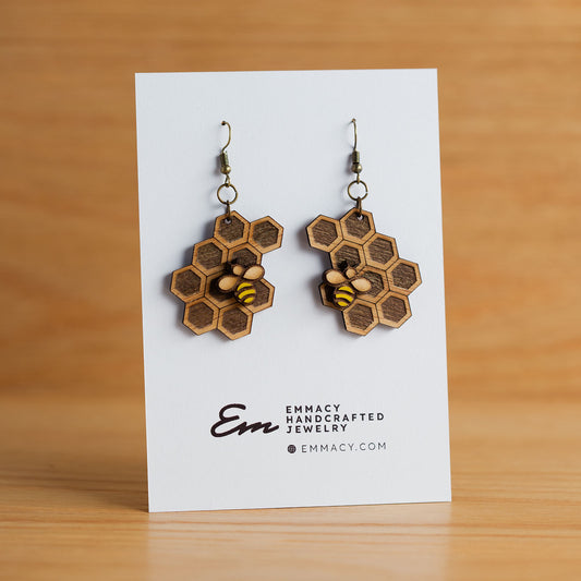 Laser cut wooden dangle earrings in the shape of a honeycomb with a paint bee attached.