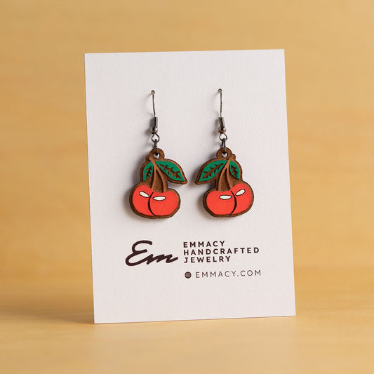 Laser cut wooden dangle earrings in the shape of a cherry painted red with green leaves.