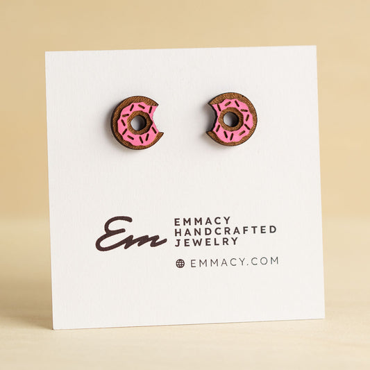 Laser cut wooden stud earring cut in the shape of a donut with a bite taken out painted pink with sprinkles.