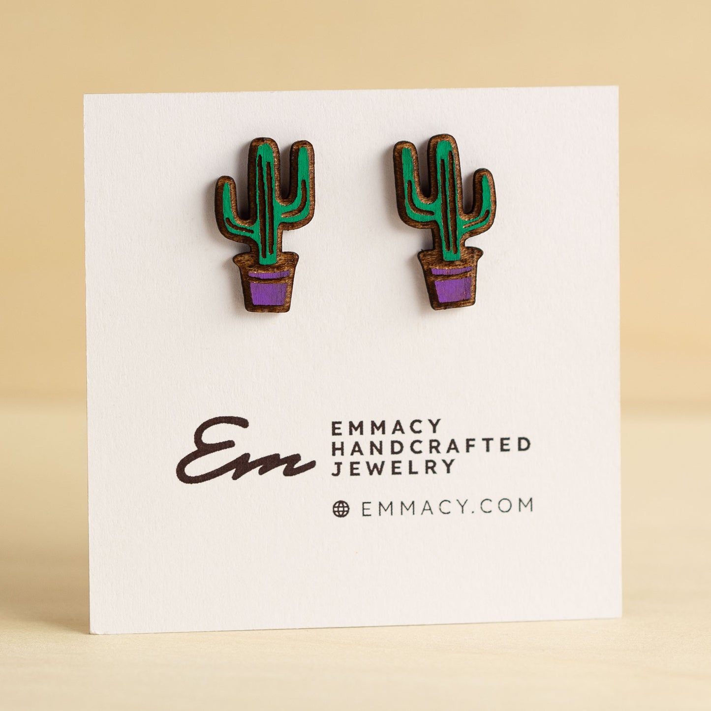 Laser cut wooden stud earrings cut in the shape of a potted cactus painted green and purple.