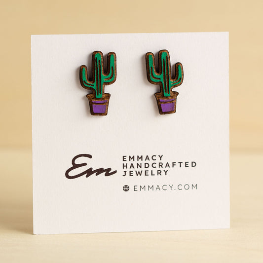 Laser cut wooden stud earrings cut in the shape of a potted cactus painted green and purple.
