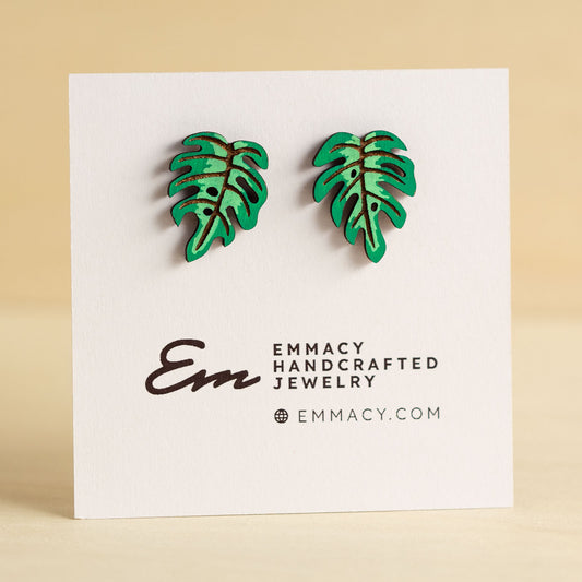 Laser cut wooden stud earrings in the shape of a monstera plant leaf painted green.
