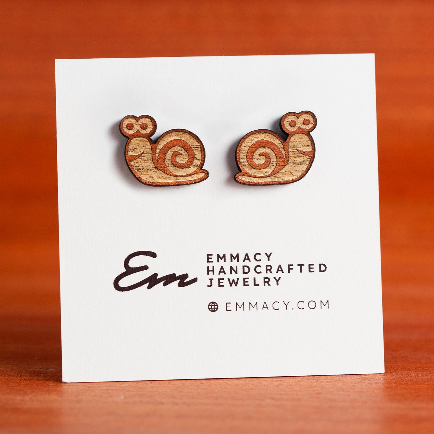 Laser cut wooden stud earrings in the shape of a snail with engraved details.